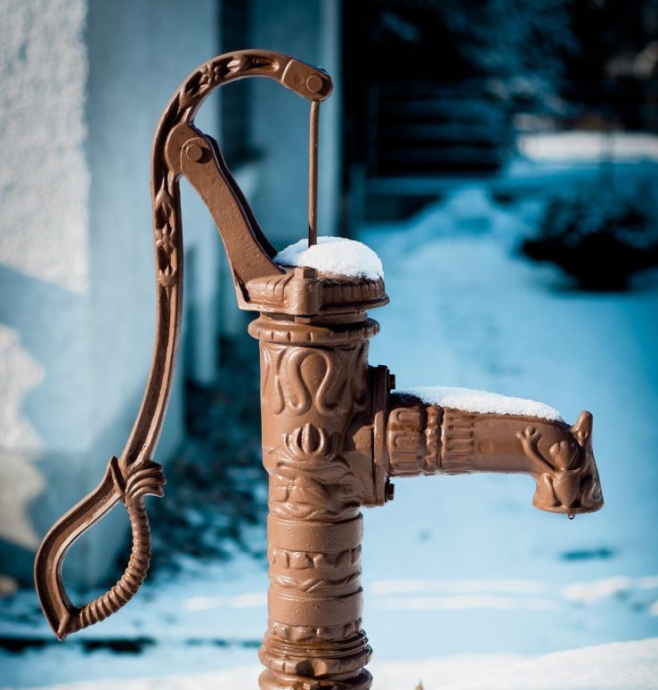 Old hand water pump in winter snow